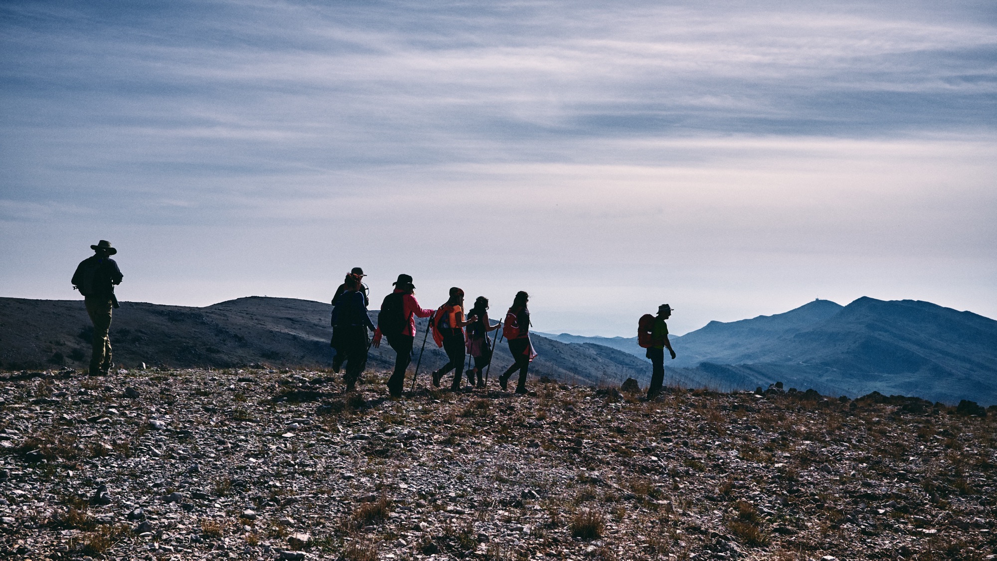 Hikers in single file along a ridge, with layers of mountains in the distance